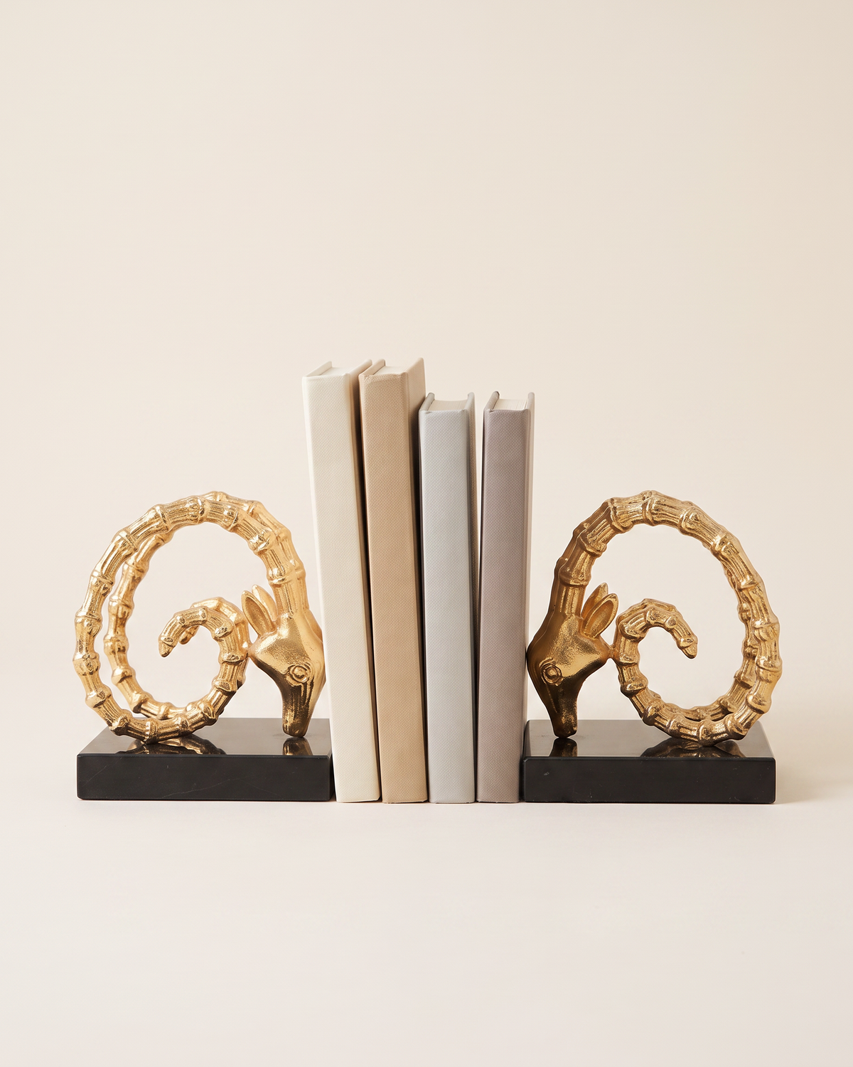 Golden Ram Horn Bookends with Black Marble Base - studio view on ivory background, holding a row of plain books