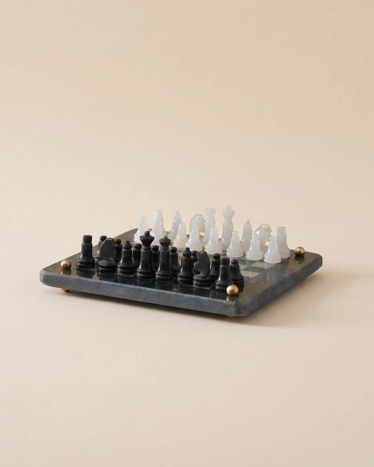 Marble Chess Set - black and white marble chess pieces on a dark marble board with brass feet, ivory studio background