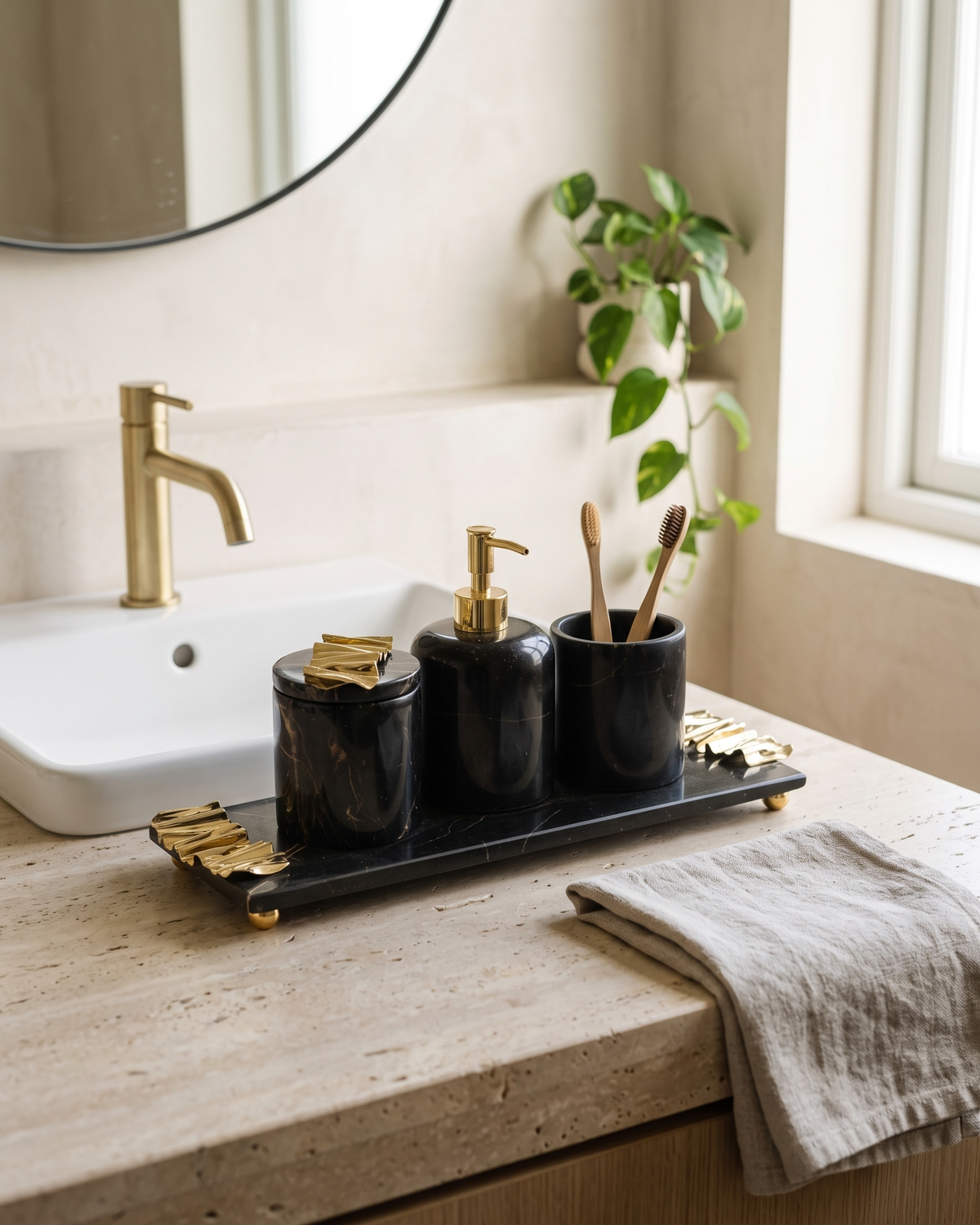 Black marble bath set with gold wave accents arranged on a travertine vanity counter beside a basin