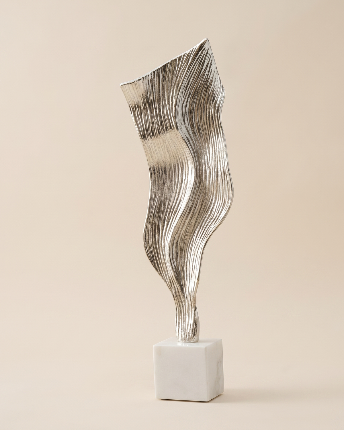 Wind Decorative Object II - striated silver draped sculpture on white marble cube, ivory studio background
