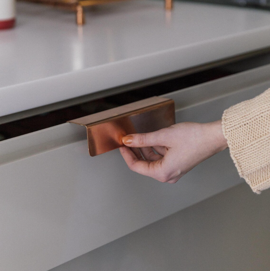 Brushed copper finger pull handle on a cabinet drawer, featuring a sleek and minimalist design made from solid copper.