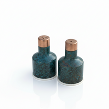 Two ceramic salt and pepper shakers with blue speckled design and copper lids on a white background.