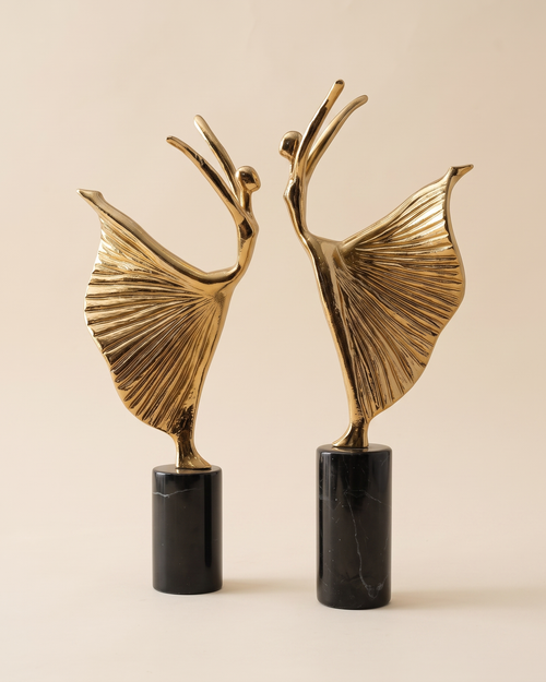 Ballerina Decorative Object VI - two gold brass dancer sculptures with pleated skirts on black marble bases, ivory studio background