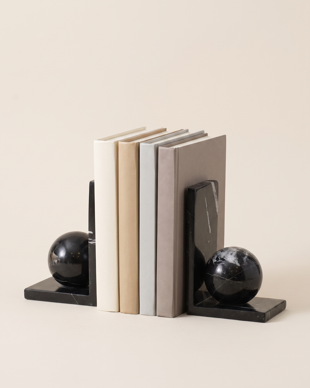 Black Marble Sphere Bookends - studio view on ivory background, holding a row of plain books