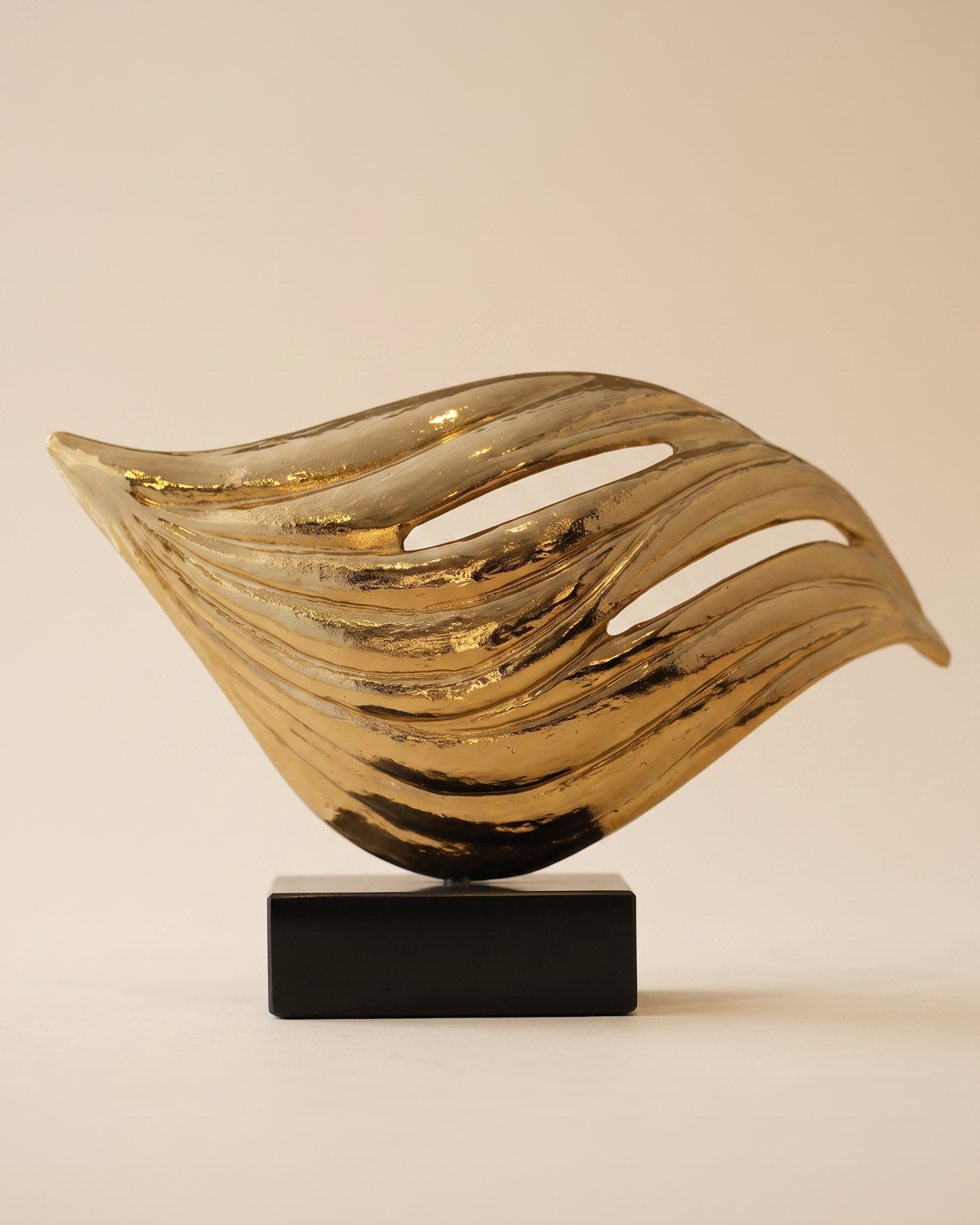 Brass wave sculpture on a black marble base, pale ivory studio background