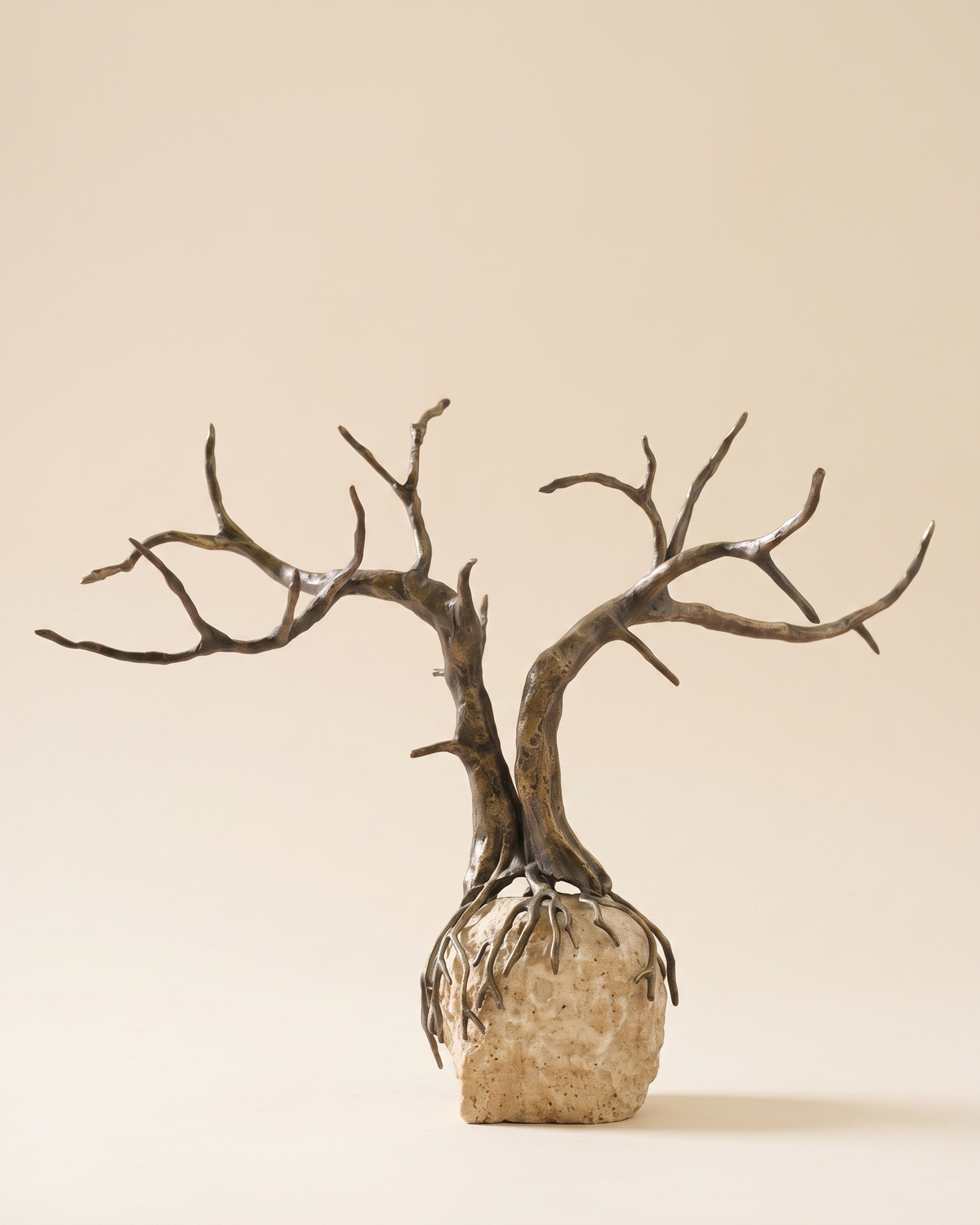 Dry Tree Decorative Object - bare antiqued bronze tree on travertine boulder base, ivory studio background