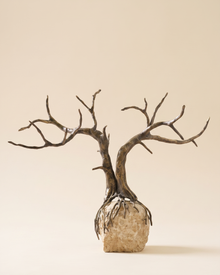 Dry Tree Decorative Object - bare antiqued bronze tree on travertine boulder base, ivory studio background