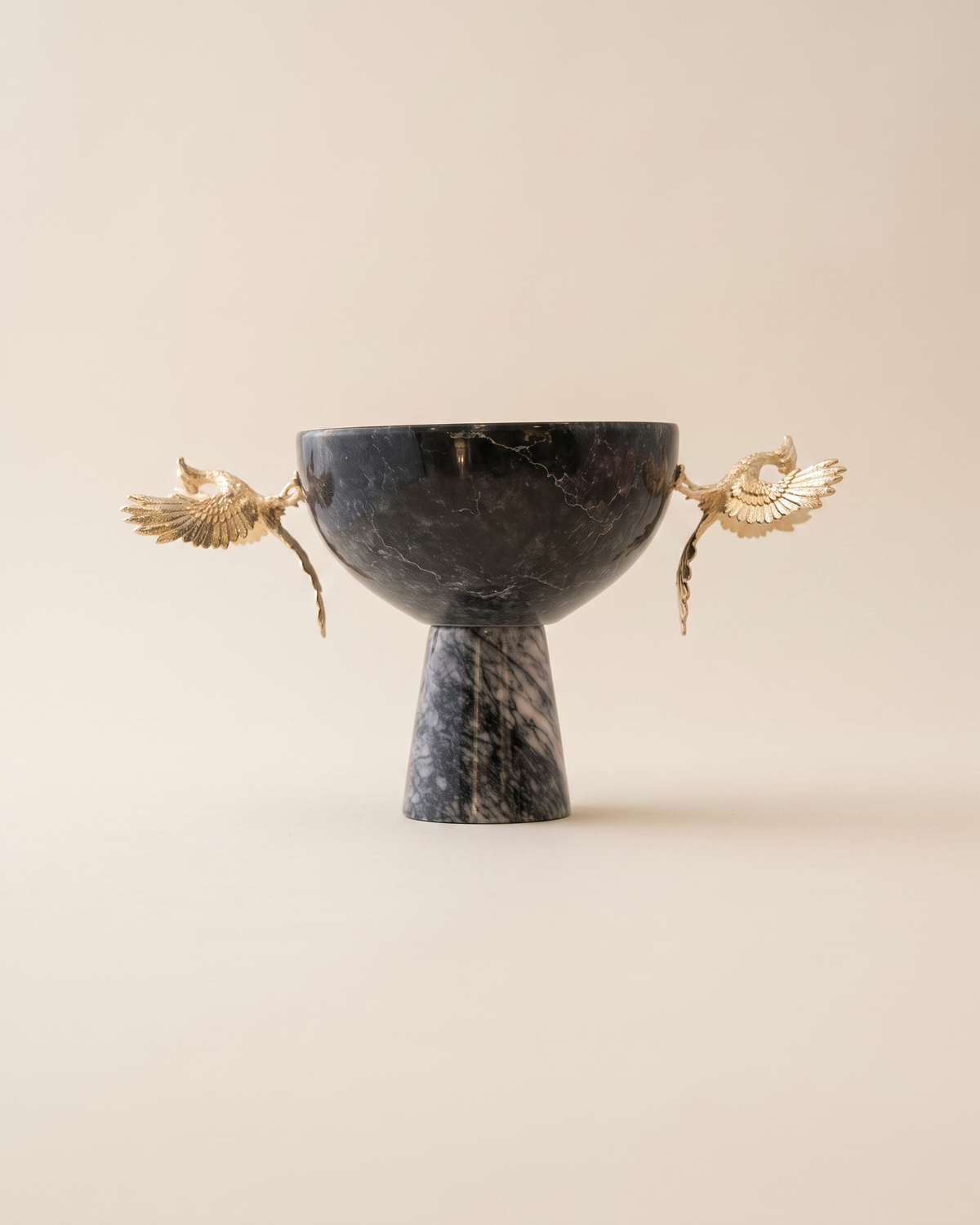 Footed bowl with two gold phoenix figures in dark veined marble on a pale ivory studio background