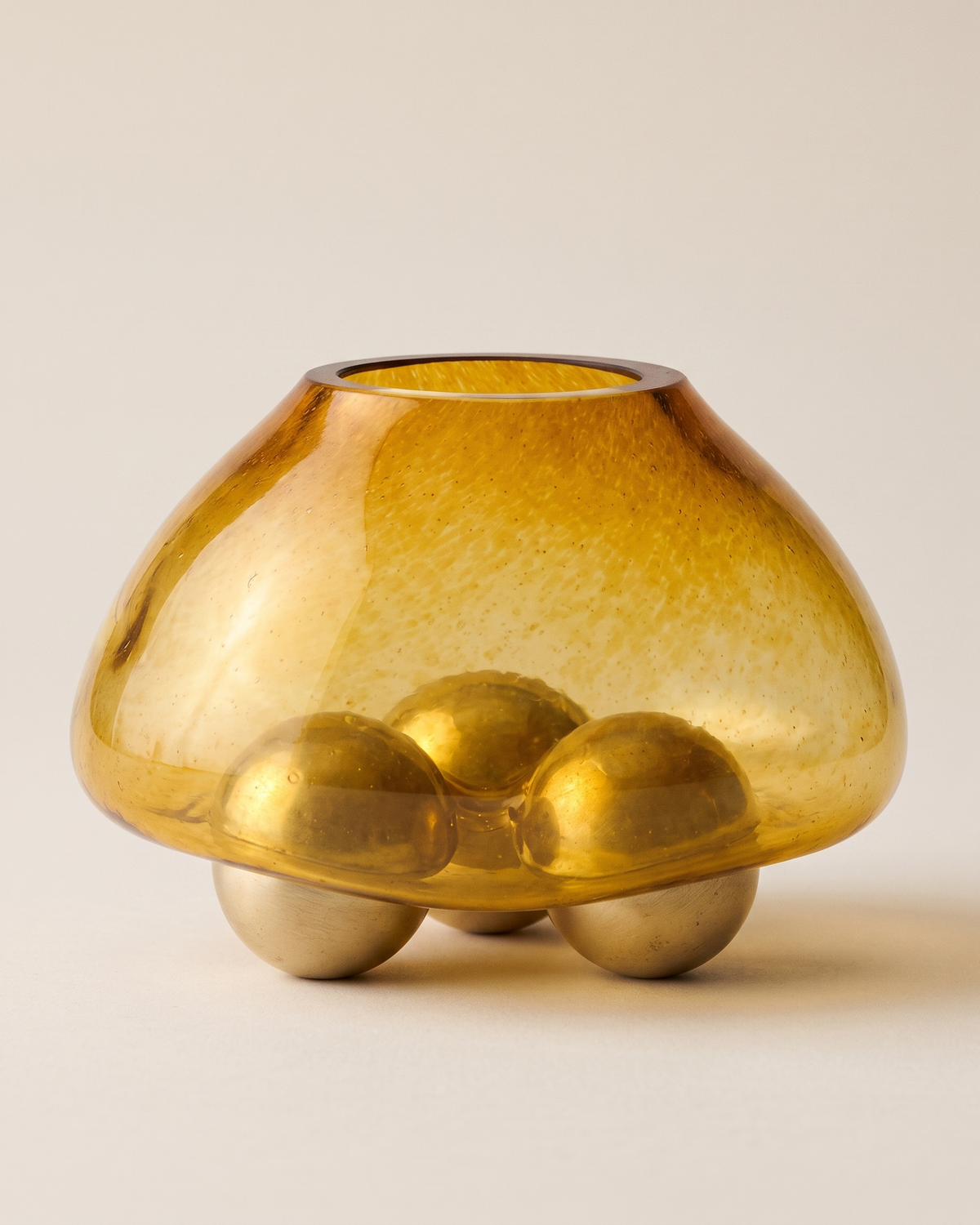 Glass Bowl with Three Brass Spheres on a pale ivory studio background