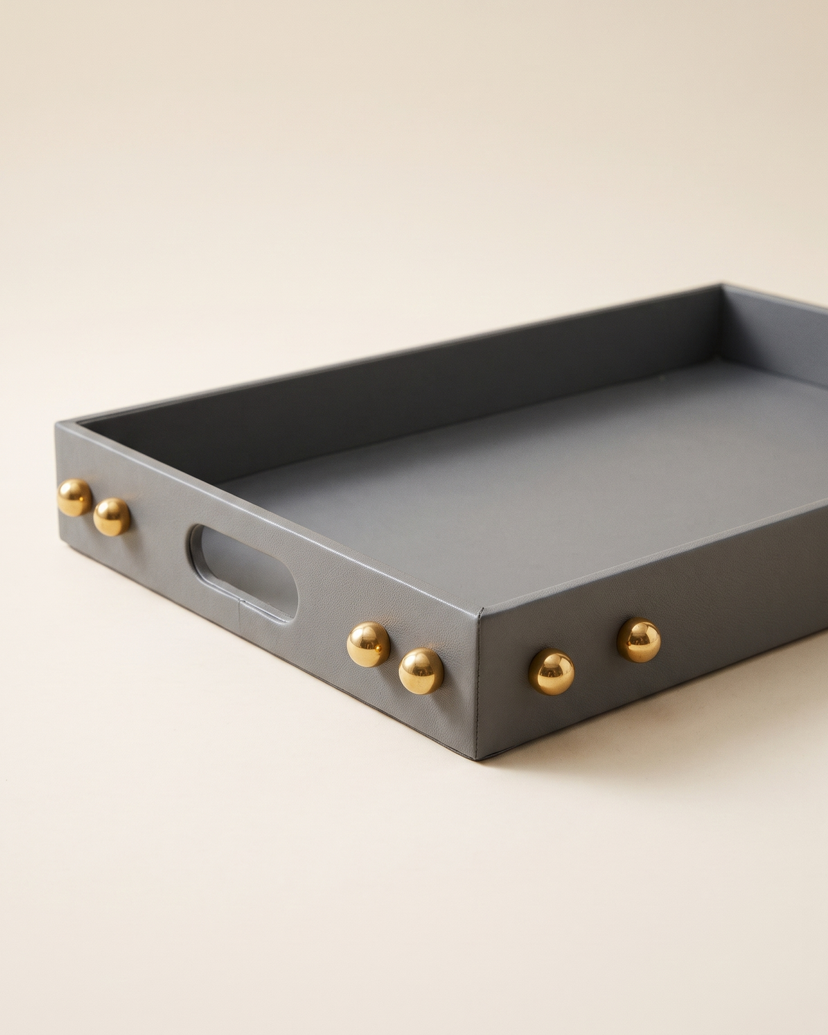 Grey leather tray with brass sphere studs, pale ivory studio background