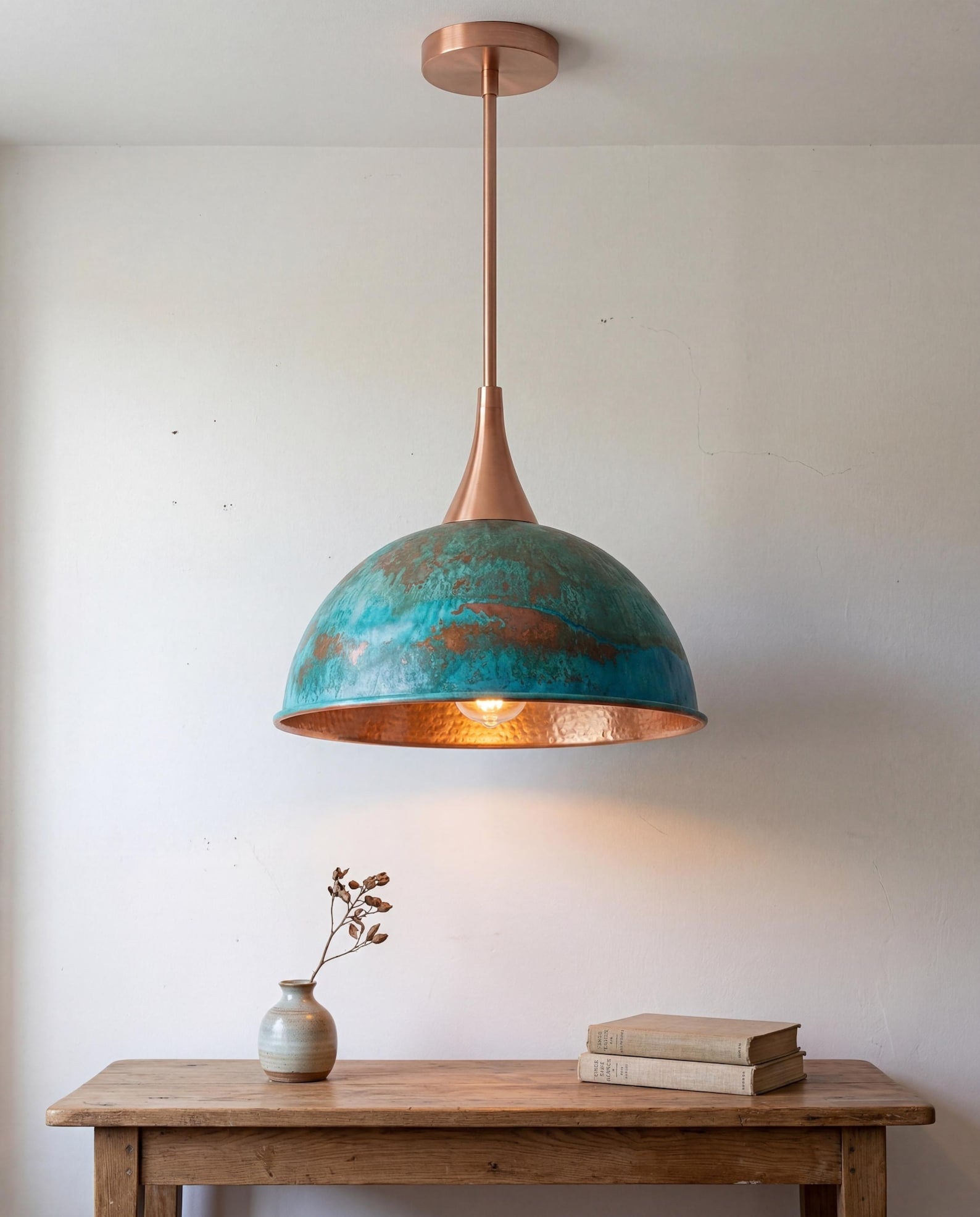 Pendant light with turquoise shade and copper accents hanging above a wooden table.