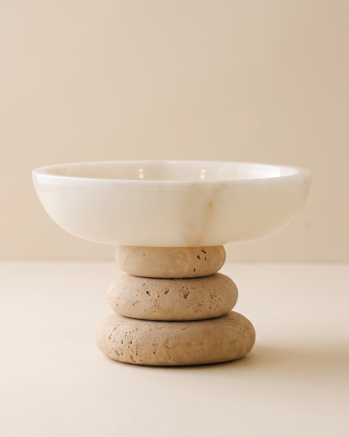 White marble bowl on a stacked travertine base, pale ivory studio background