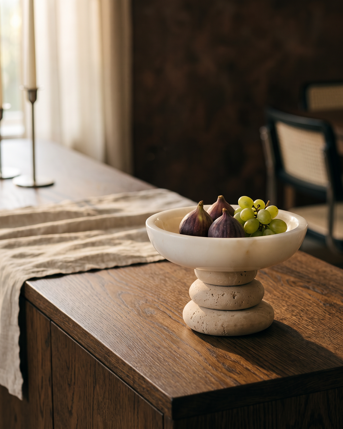White marble bowl on a travertine base holding figs on a dining sideboard