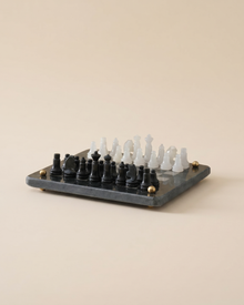 Marble Chess Set - black and white marble chess pieces on a dark marble board with brass feet, ivory studio background