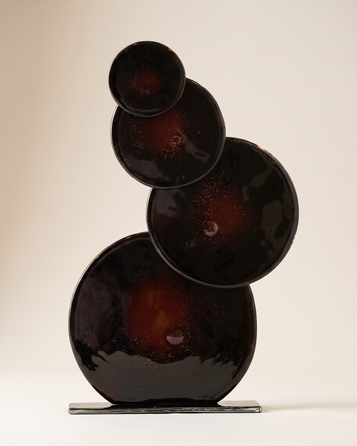 Quadruple glass bubble sculpture in dark glass, pale ivory studio background