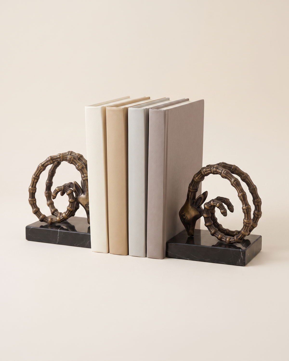 Ram Horn Bronze Bookends with Black Marble Base - studio view on ivory background, holding a row of plain books
