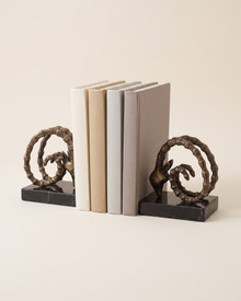 Ram Horn Bronze Bookends with Black Marble Base - studio view on ivory background, holding a row of plain books