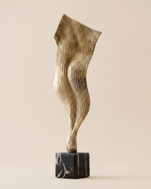 Wind Decorative Object Gold - striated gold brass draped sculpture on black marble cube, ivory studio background